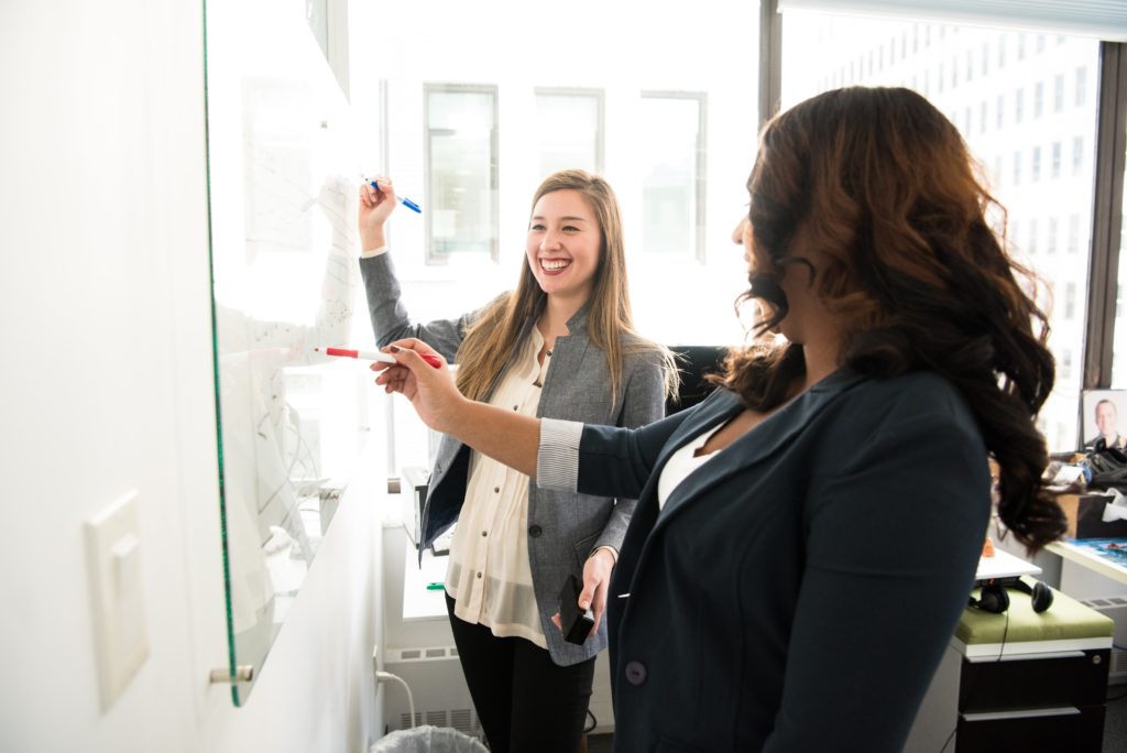 two business women writing on a white board 