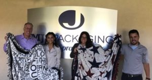 volunteers holding up some of the blankets they made for a charity their company partners with. 