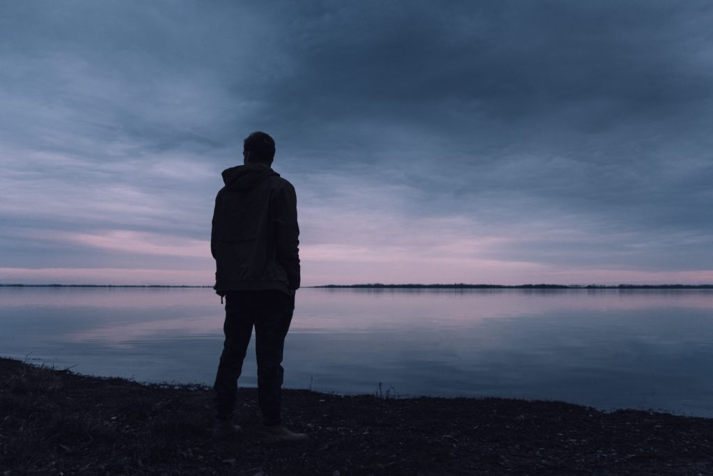 man standing at a lake during a sunset 