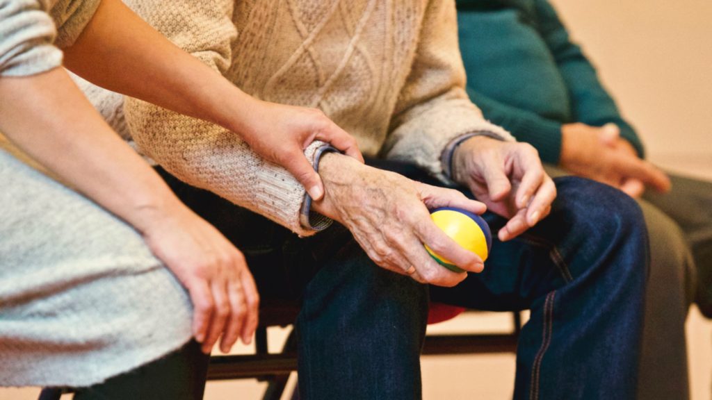 close up of a woman caregiver's hand helping an elderly man throw a ball