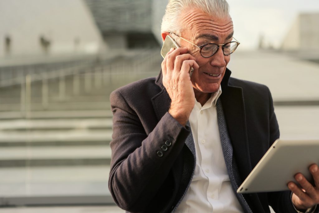 older man talking on the phone and looking at tablet