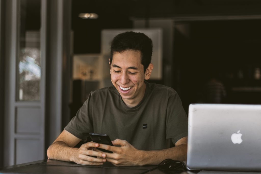 happy man looking at his phone while working on a laptop