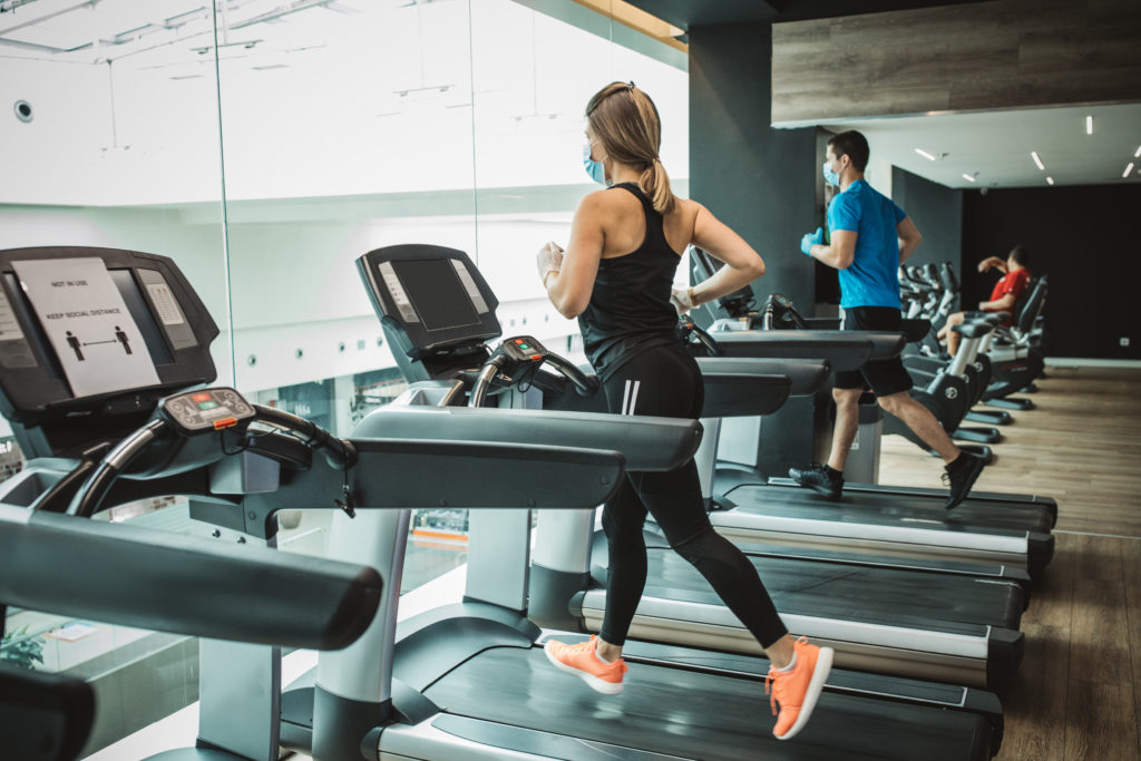 man and woman running on a treadmill at the gym while wearing masks 