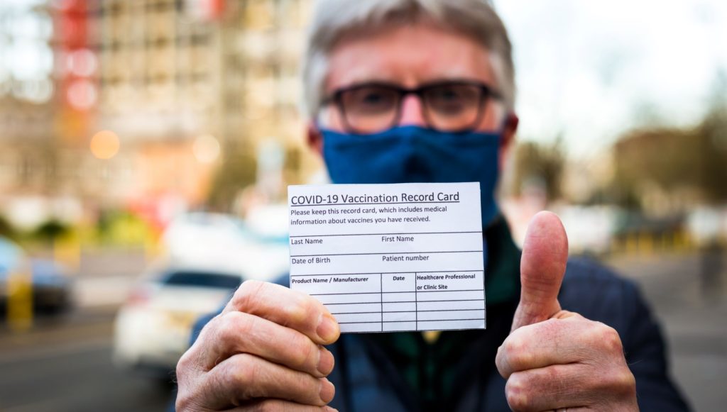 older man holding his covid-19 vaccine card 