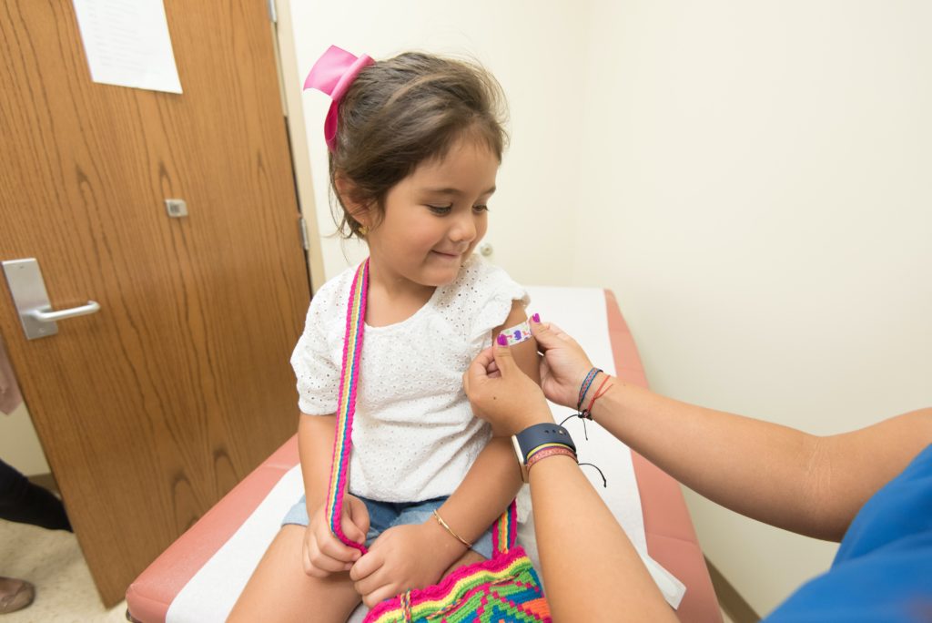 young girl receiving a vaccine, smiling 