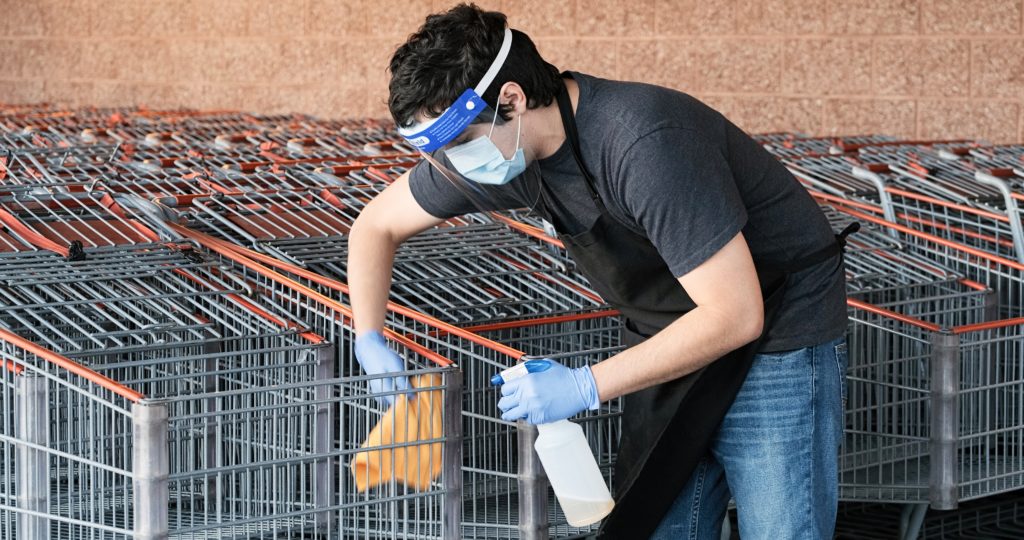 Supermarket employee wearing masks and latex gloves disinfecting shopping carts due contagion prevention